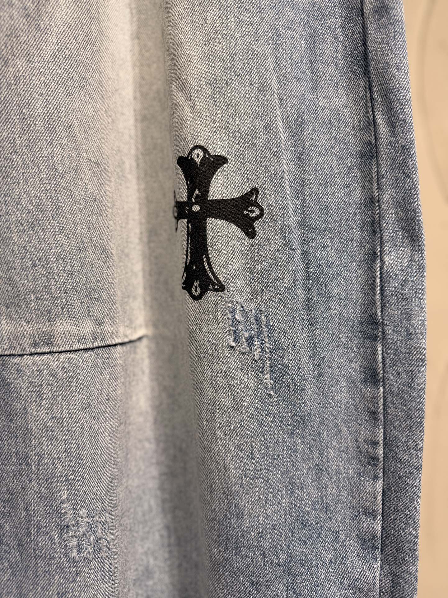 Light blue denim pants with small black cross graphic near the hem