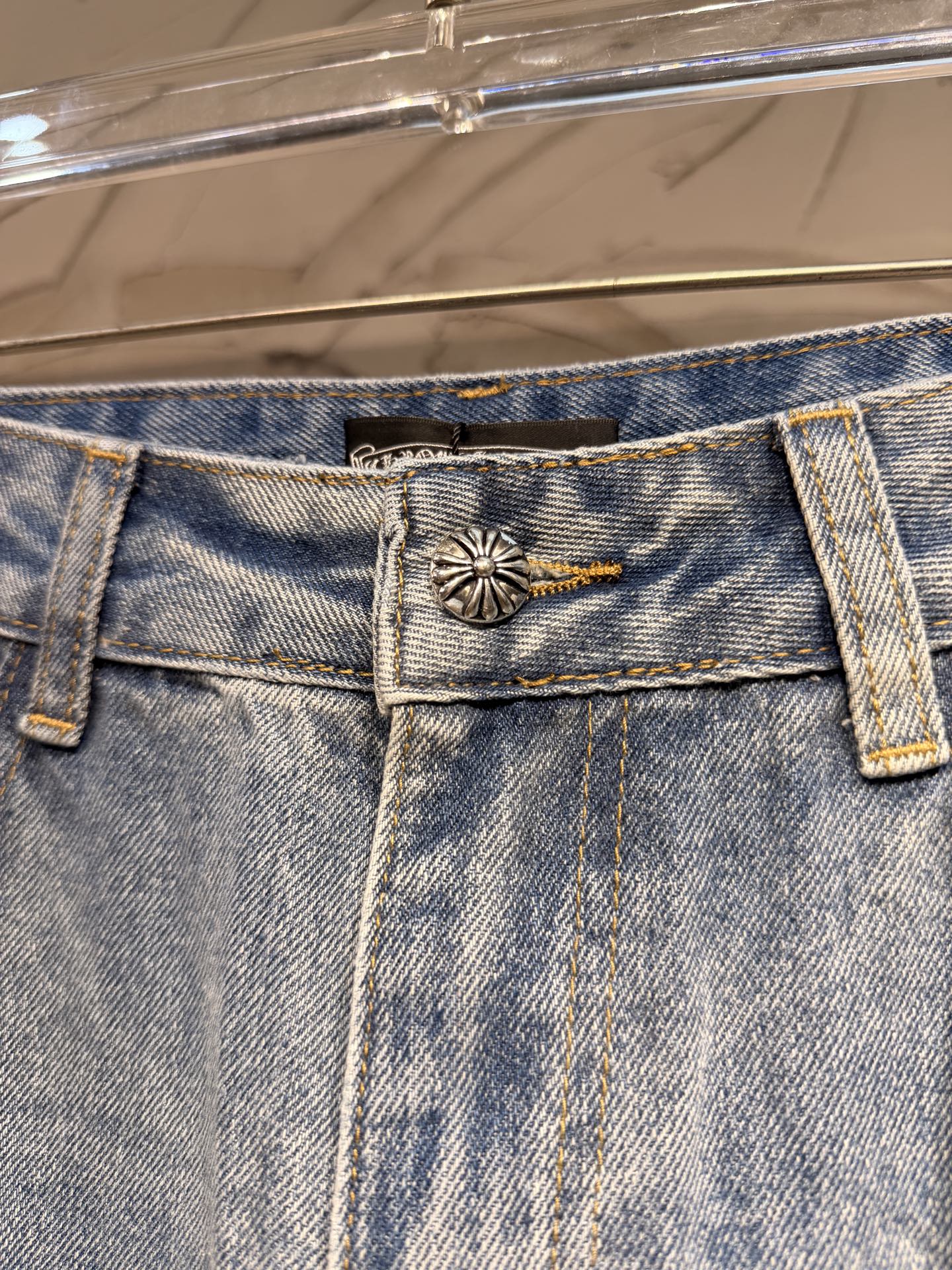 Light blue denim pants with metal-button closure and small cross emblem on waistband