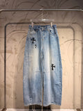 Light blue denim pants with black cross graphic patches on the front legs