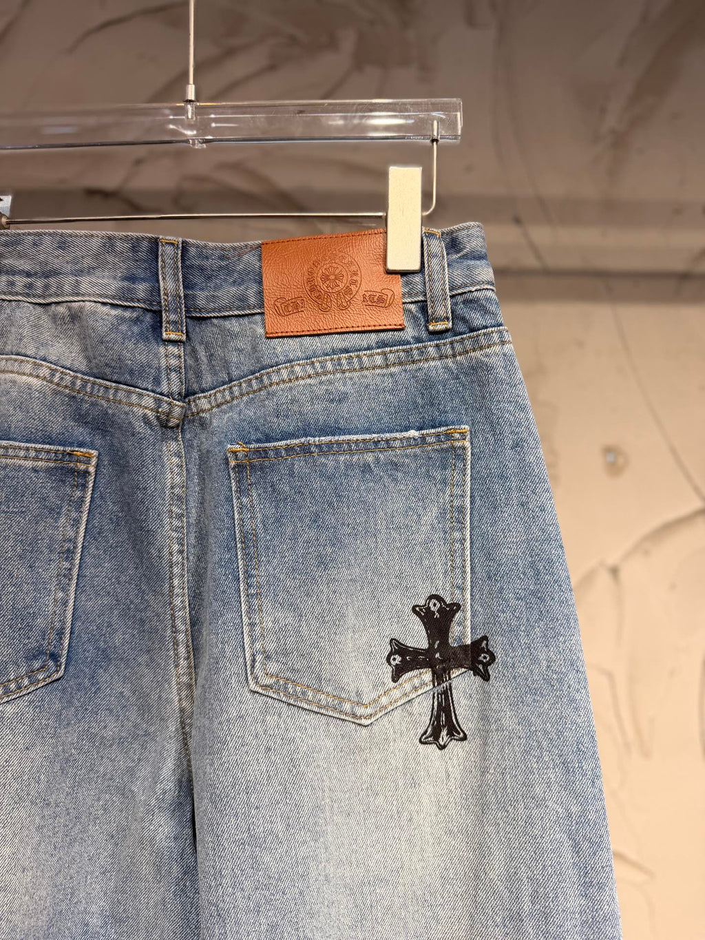 Light blue denim pants with leather-logo label and black cross patch on the pocket