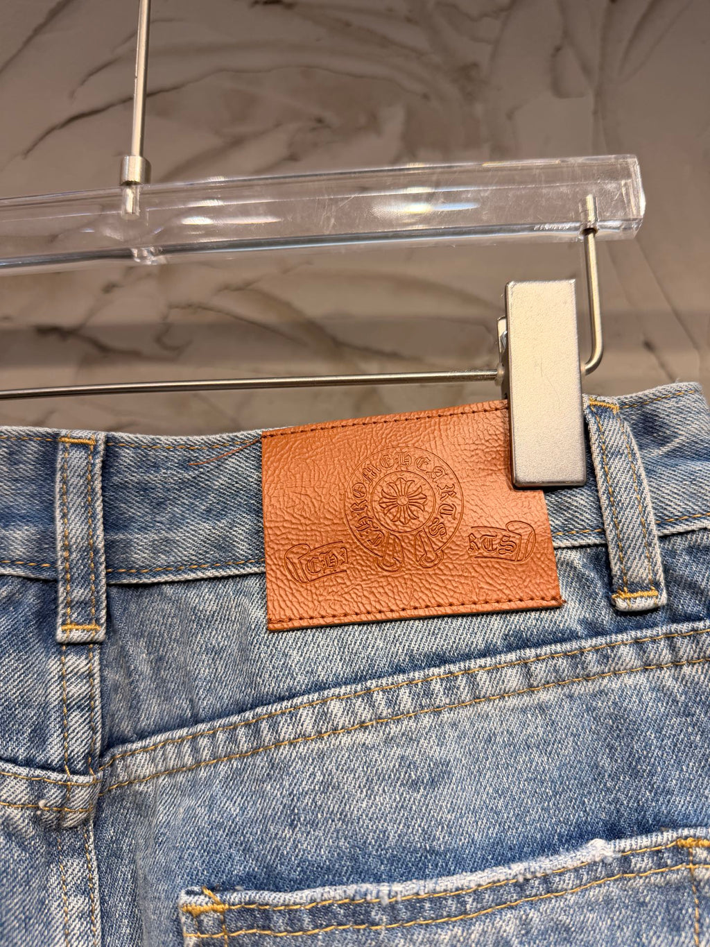 Blue denim pants waistband with brown leather logo patch and metal button