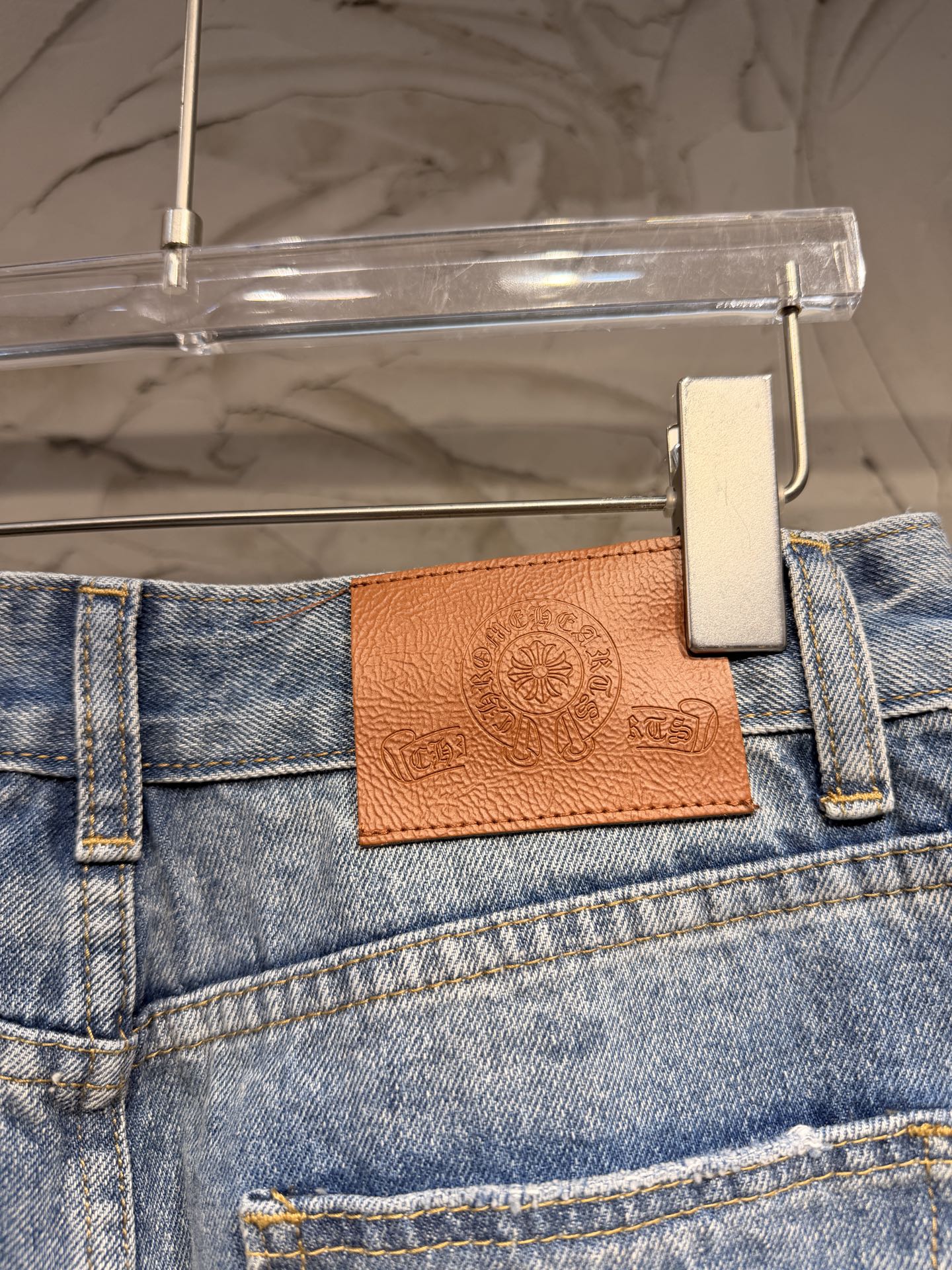 Blue denim pants waistband with brown leather logo patch and metal button