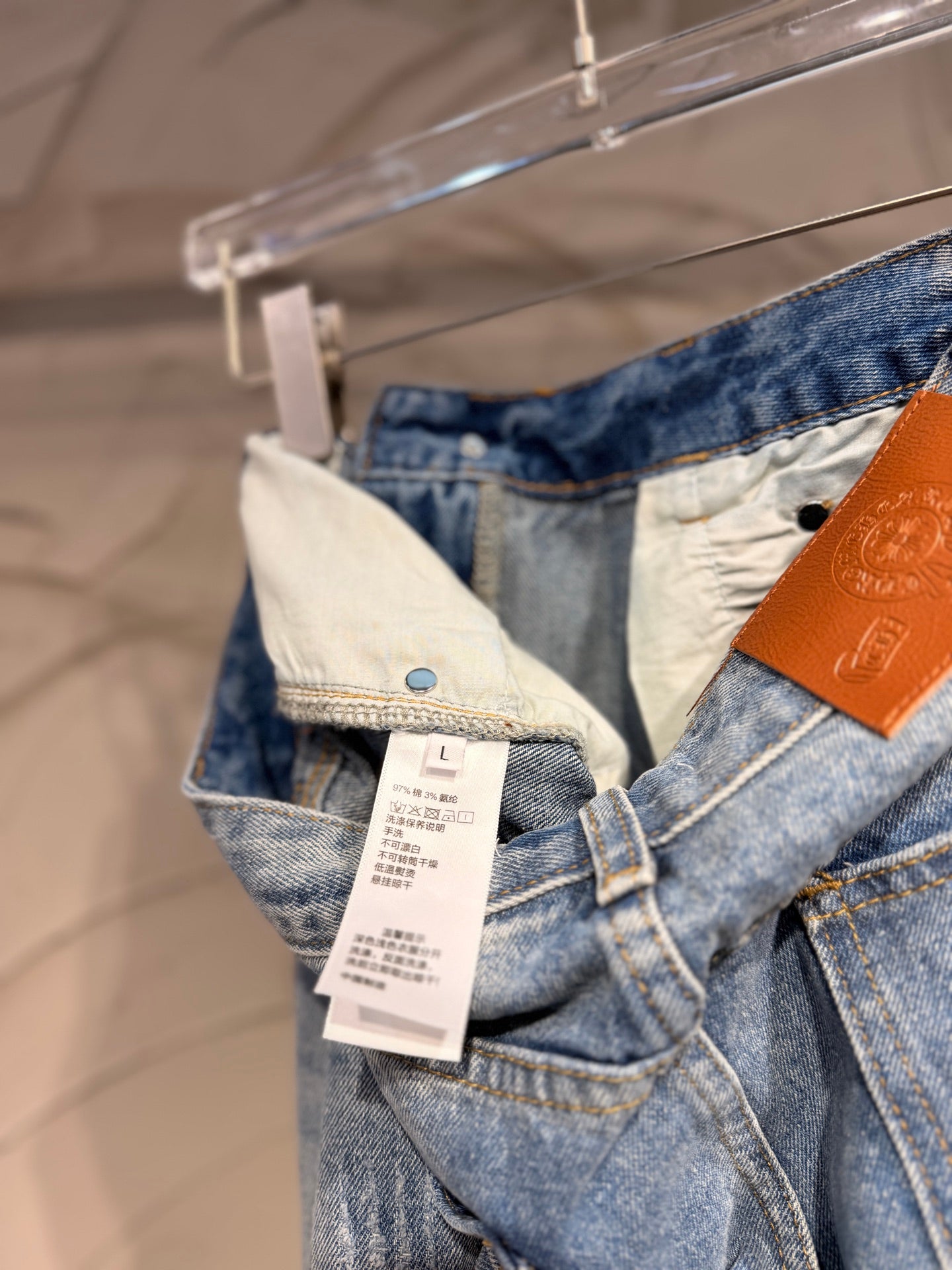 Light blue denim pants with adjustable waistband tag and cross graphic on the leg
