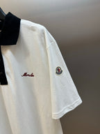 White polo shirt with script logo on chest and circular sleeve patch