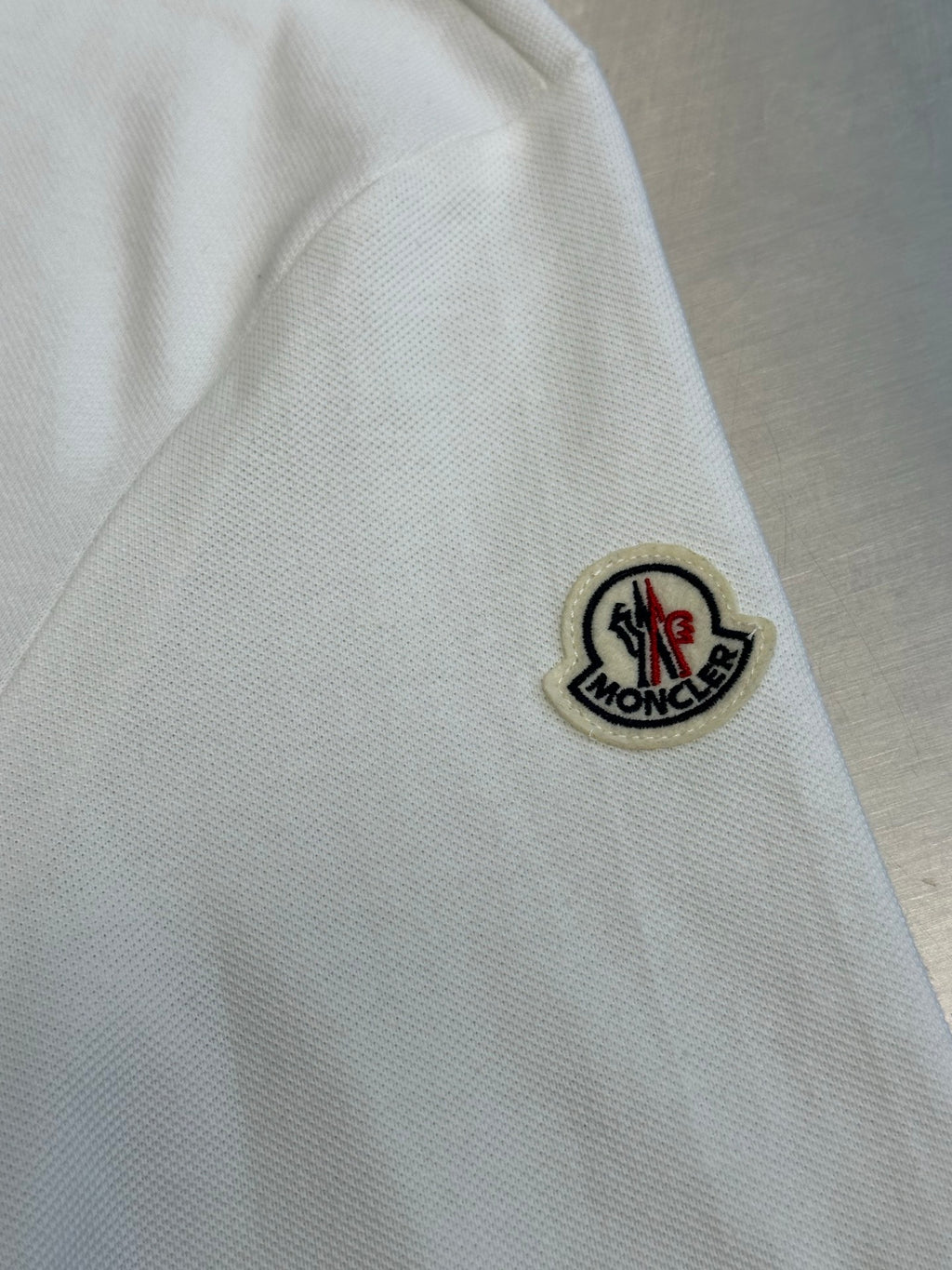 Close-up of white polo sleeve with round logo patch and black outline