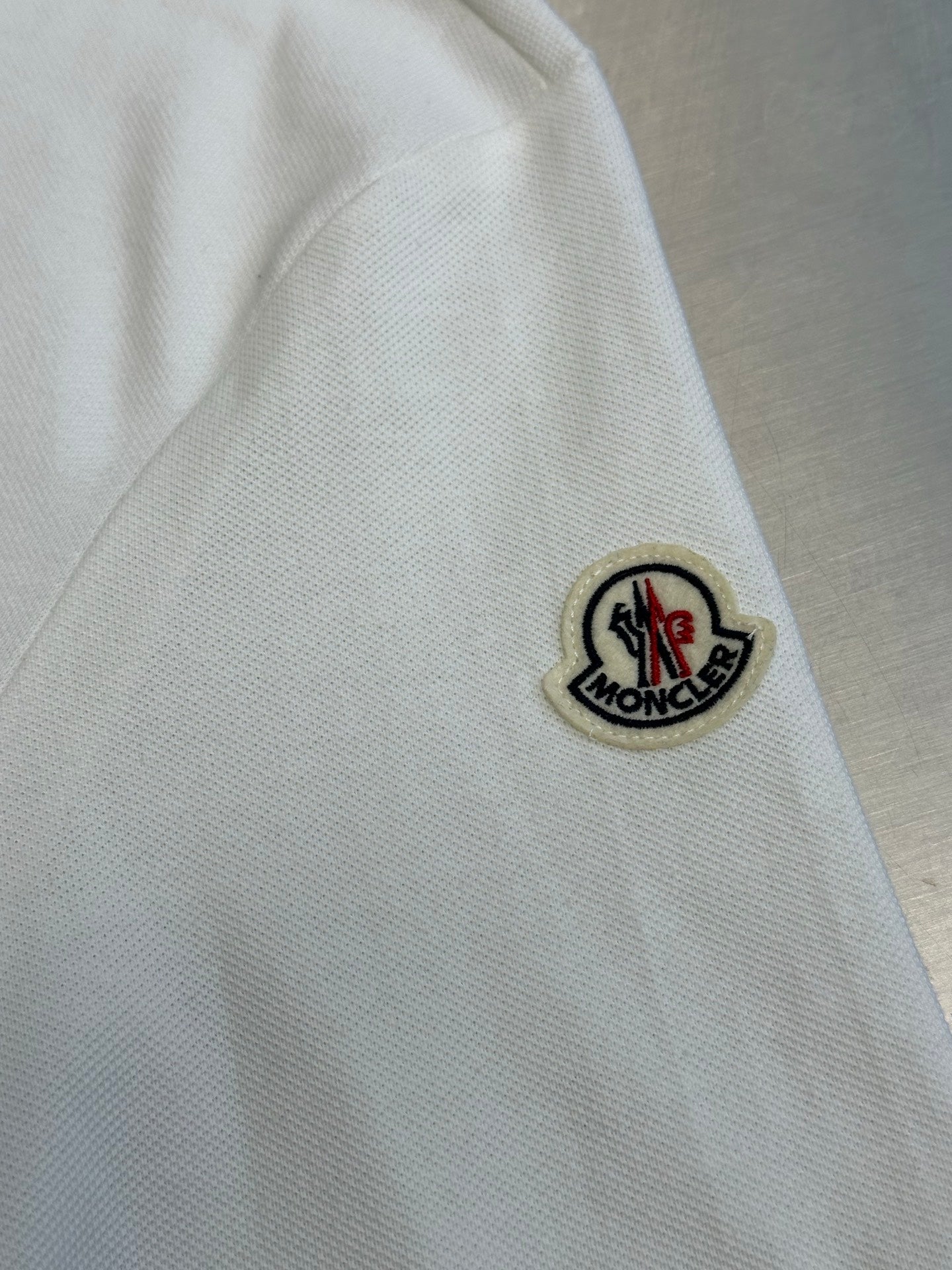 Close-up of white polo sleeve with round logo patch and black outline
