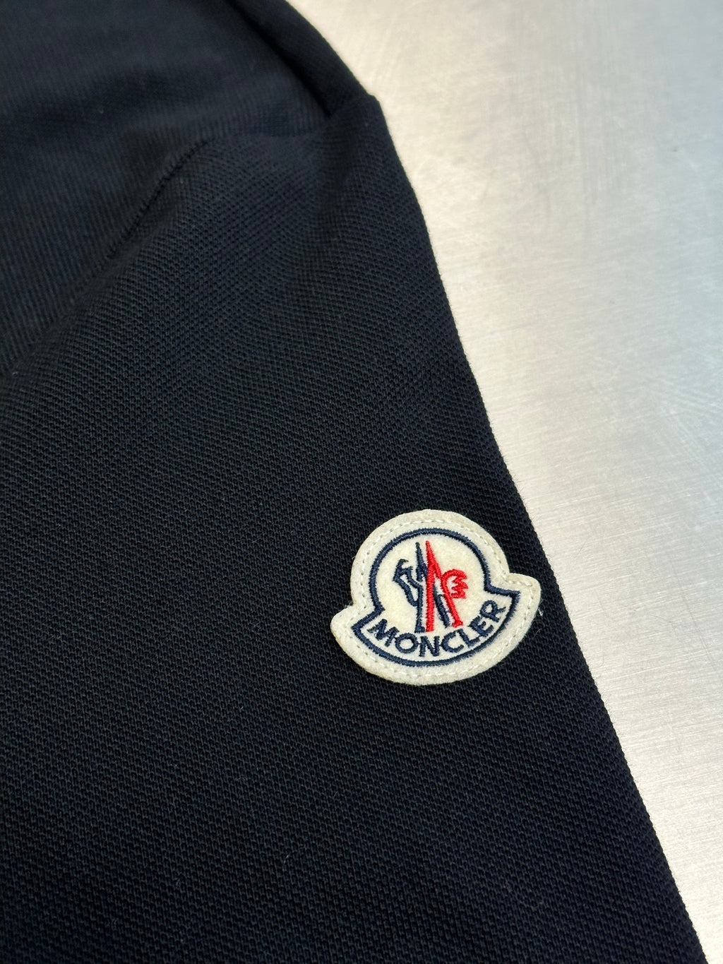Moncler sleeve patch on navy polo shirt near the shoulder seam