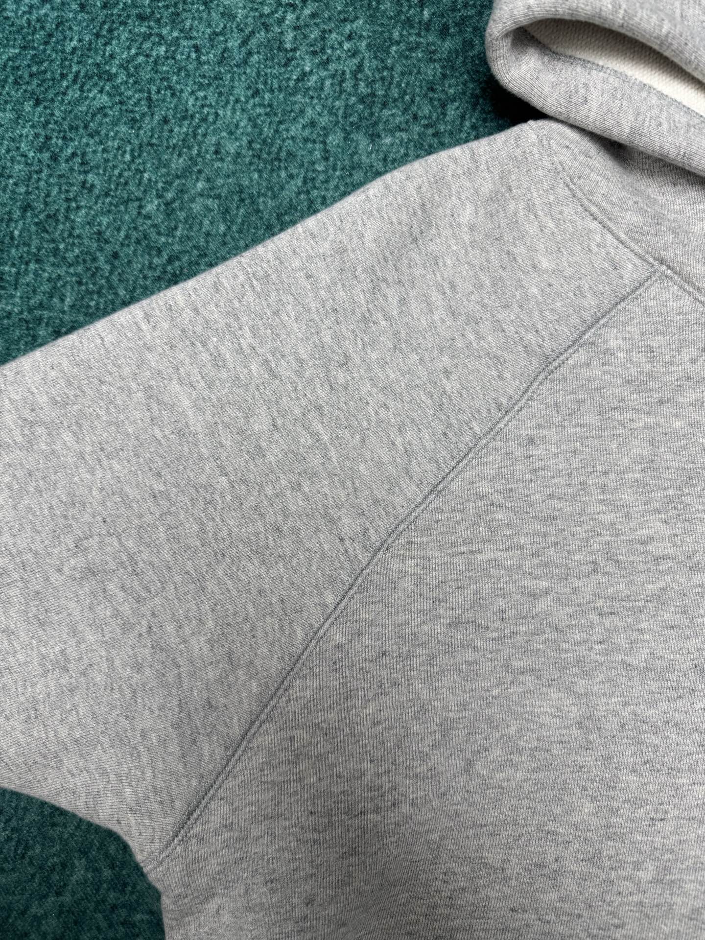 Light gray hoodie close-up with stitched hood seam and sleeve panel