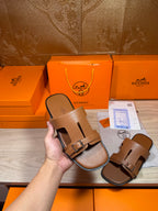 Hermes brown leather sandals held up, double strap and metal buckle, one shoe shown