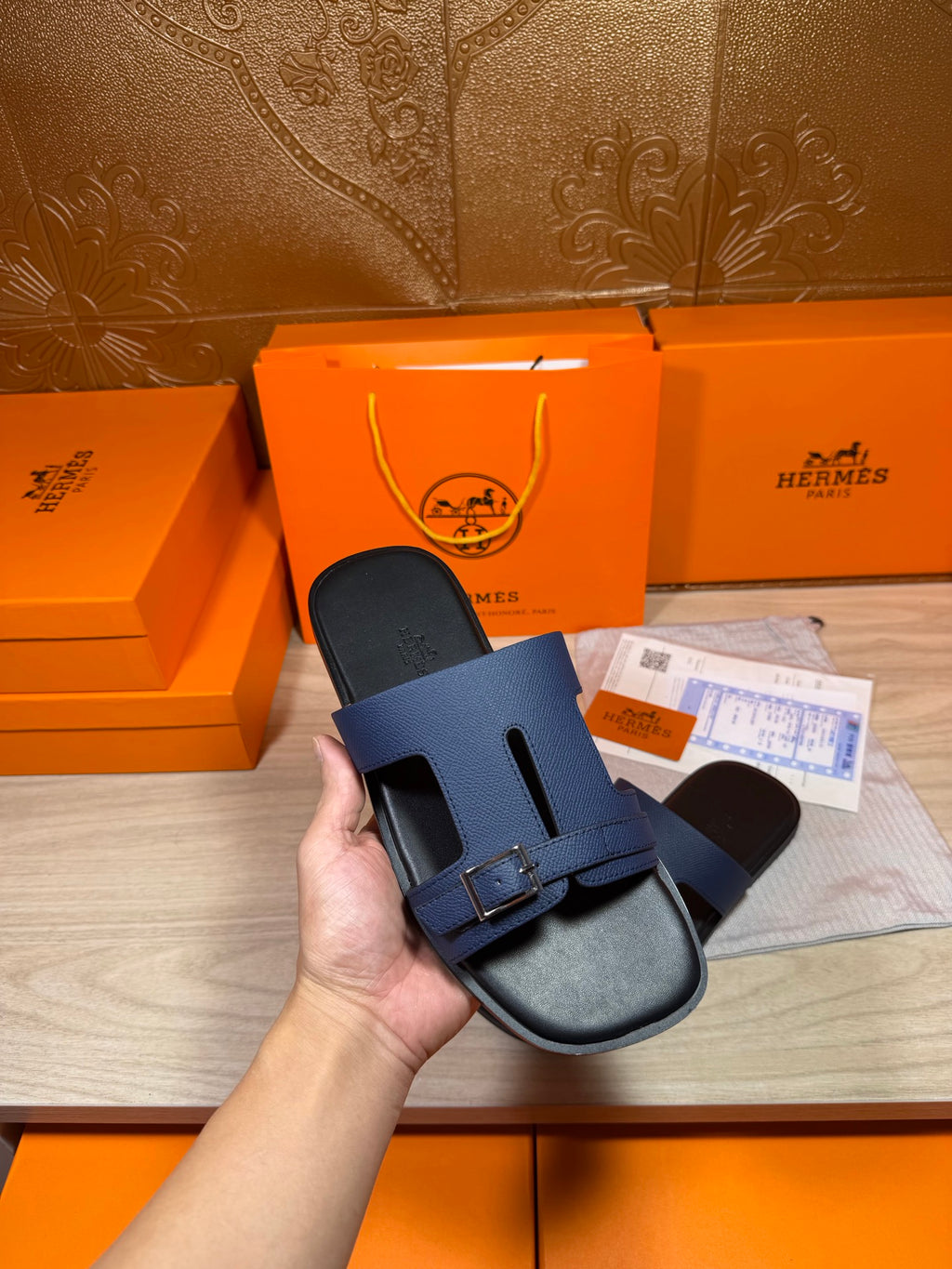 Hand-held navy slide sandals showing two straps and rectangular buckle on footbed