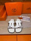 White leather slide sandals with black-trimmed edges and adjustable buckle straps
