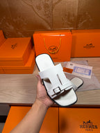 White leather slide sandal held in hand, showing front strap with buckle