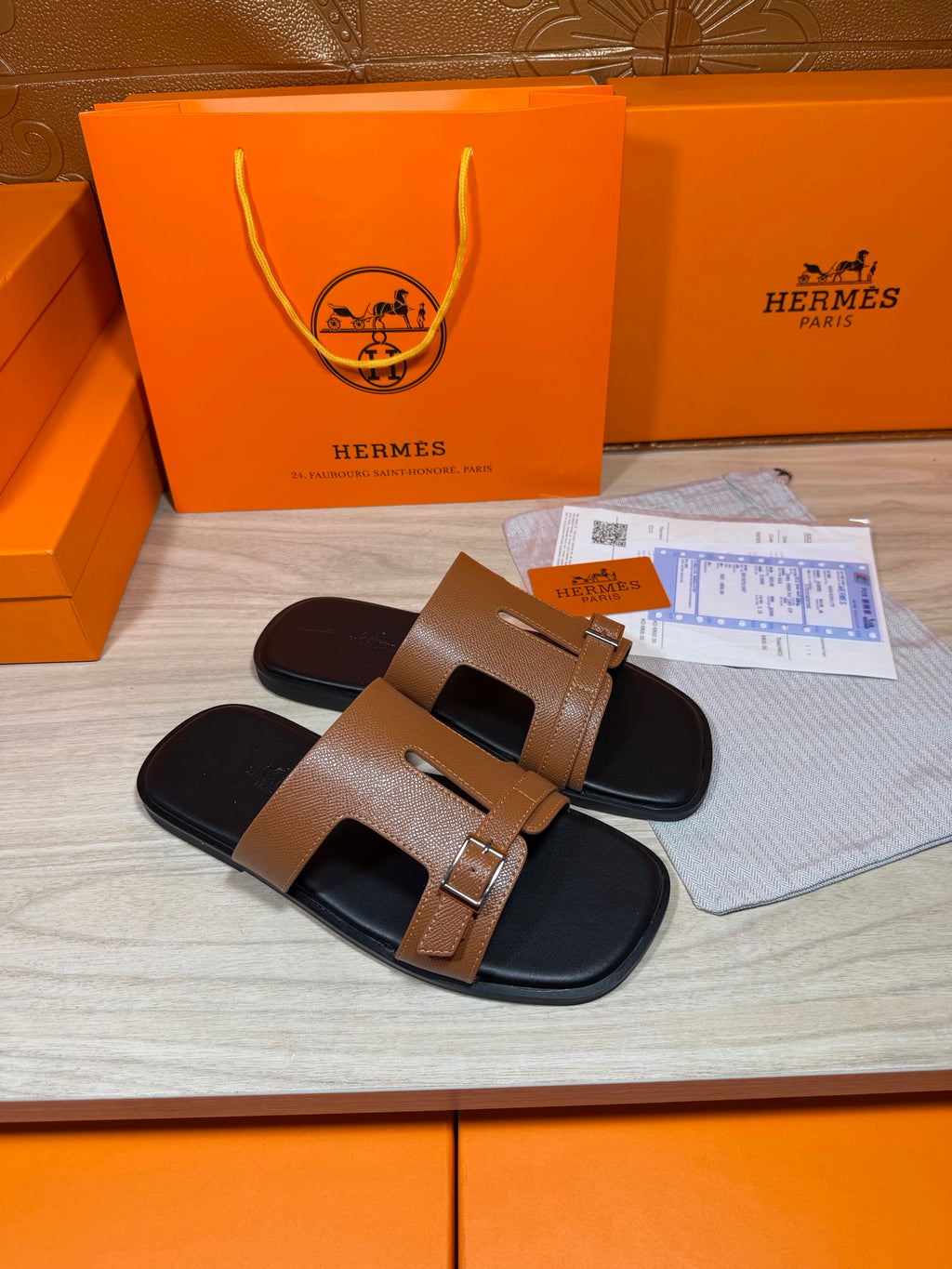 Tan leather slide sandals with gold-tone buckle and wide double straps over black footbed