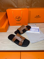 Tan leather double-strap slide sandals with gold-tone buckles on black footbeds