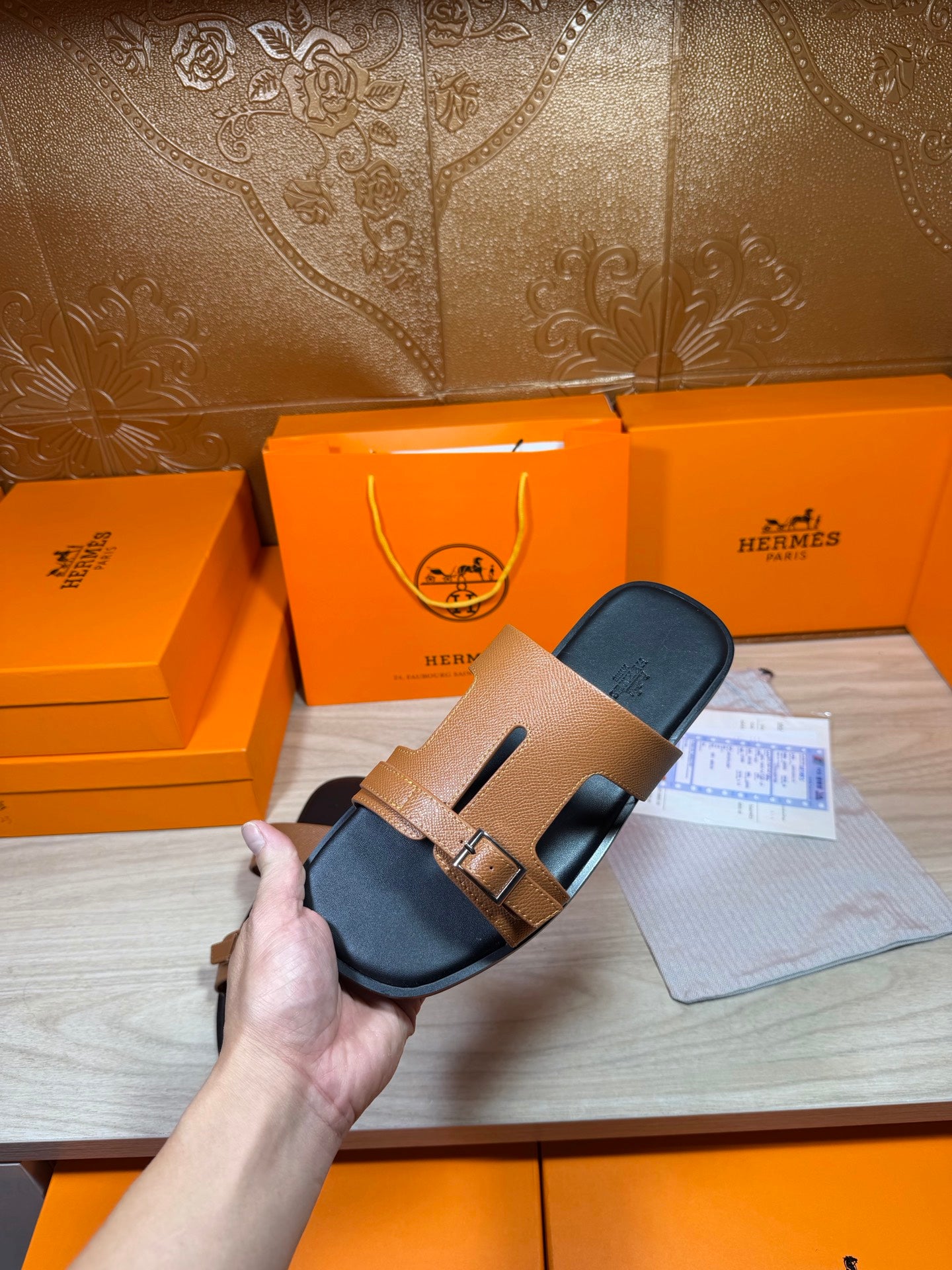 Tan leather slide sandals with gold-tone buckle strap and black footbed, side view