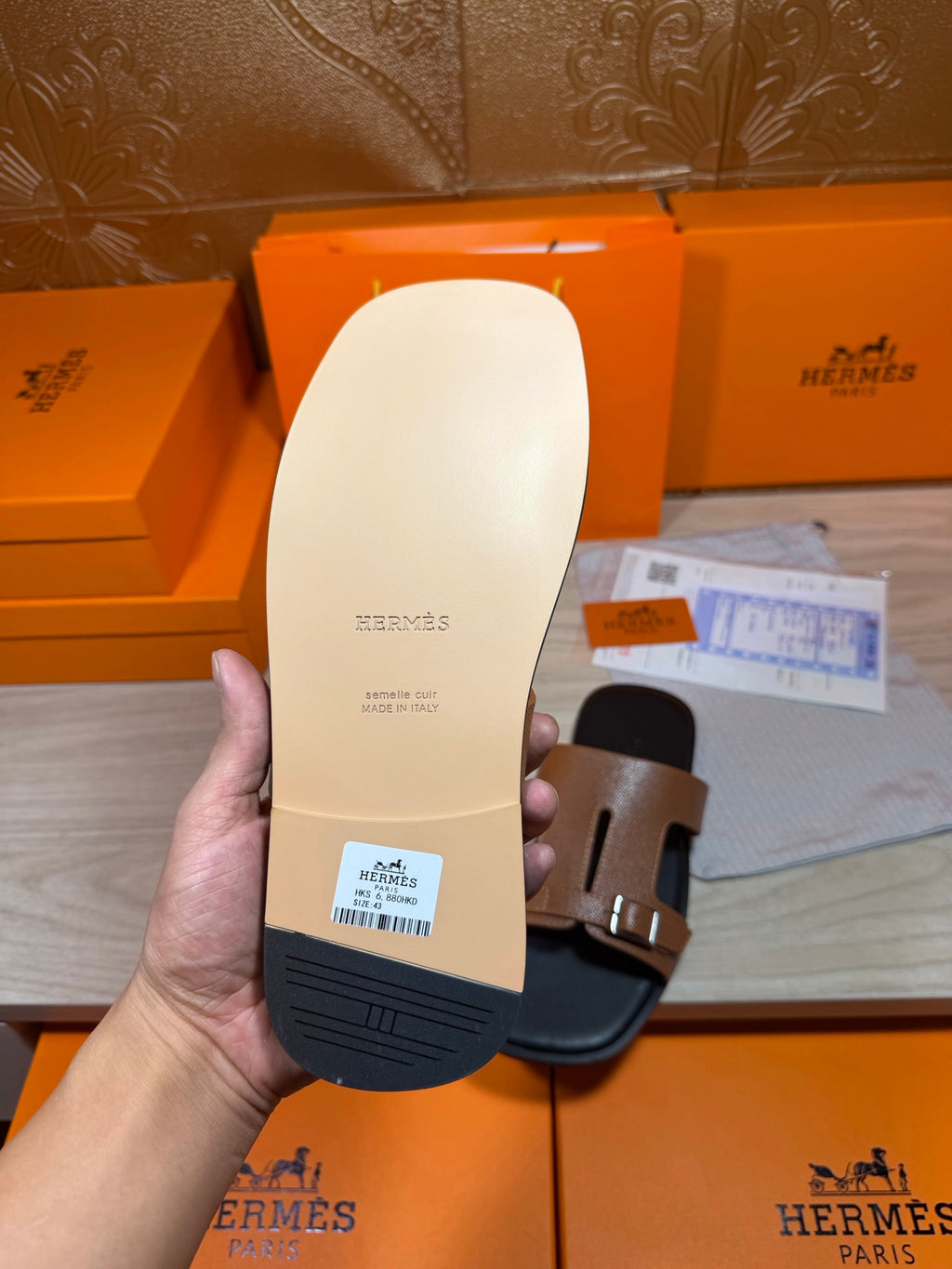 Tan slide sandal outsole with Hermes logo and black side, shown from bottom