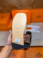 Tan slide sandal outsole with Hermes logo and black side, shown from bottom