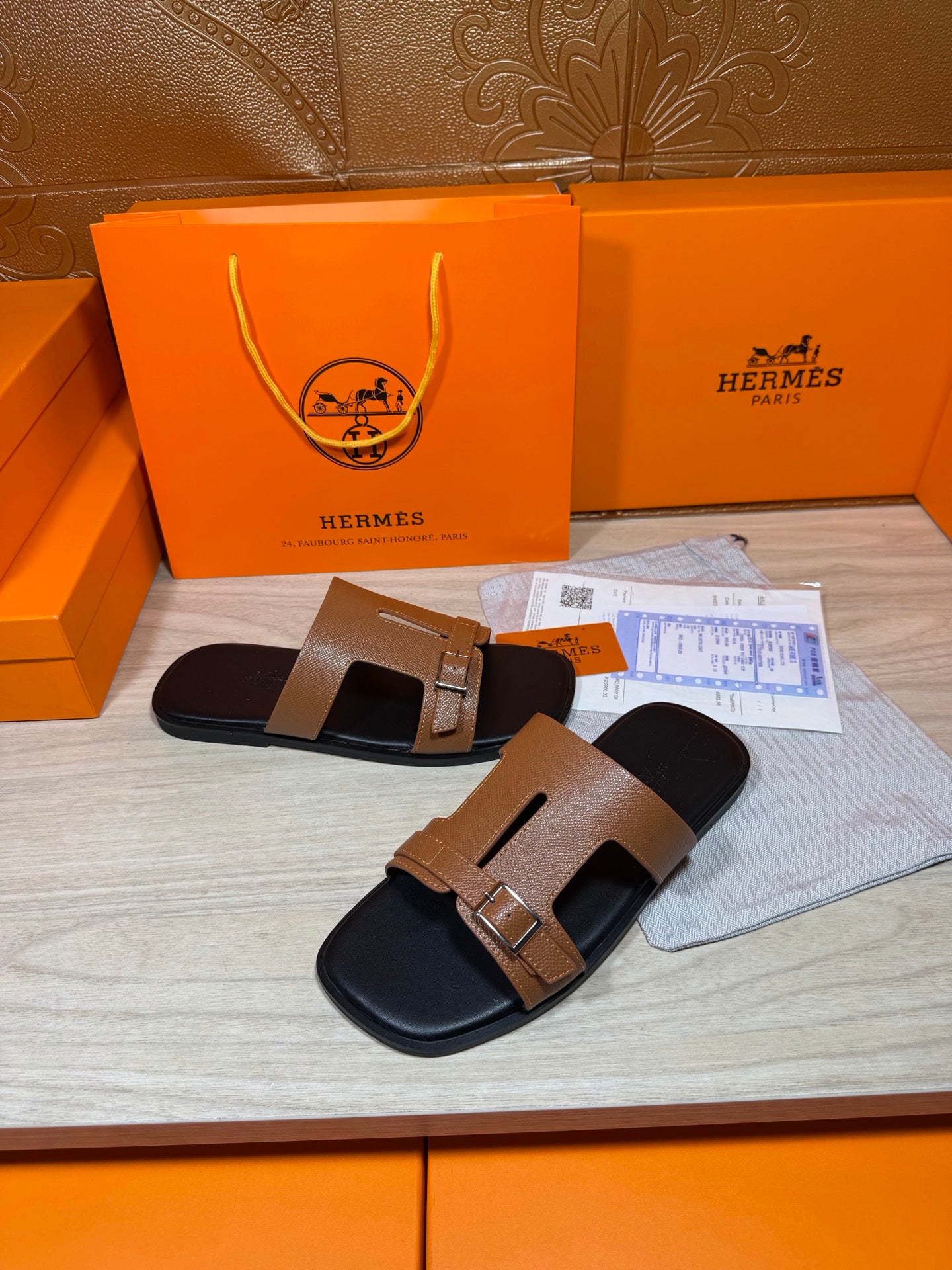 Tan leather slide sandals with gold-tone buckle hardware and black molded footbed