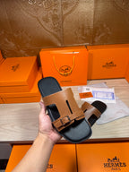 Tan leather slide sandals with gold-tone buckle and black footbed held in hand