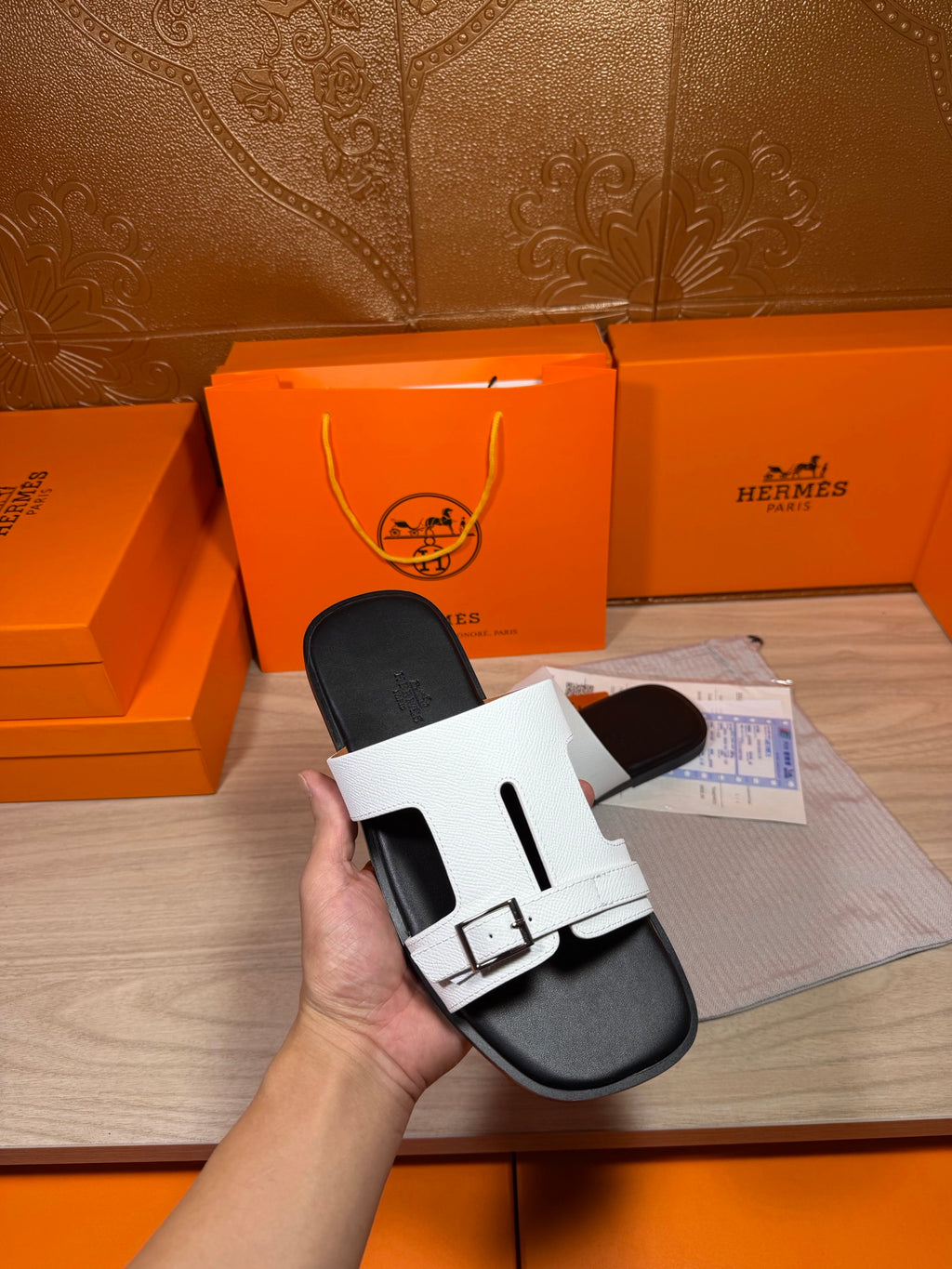 White slide sandals held in hand, black footbed with double straps and buckles