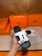 White slide sandals held in hand, black footbed with double straps and buckles