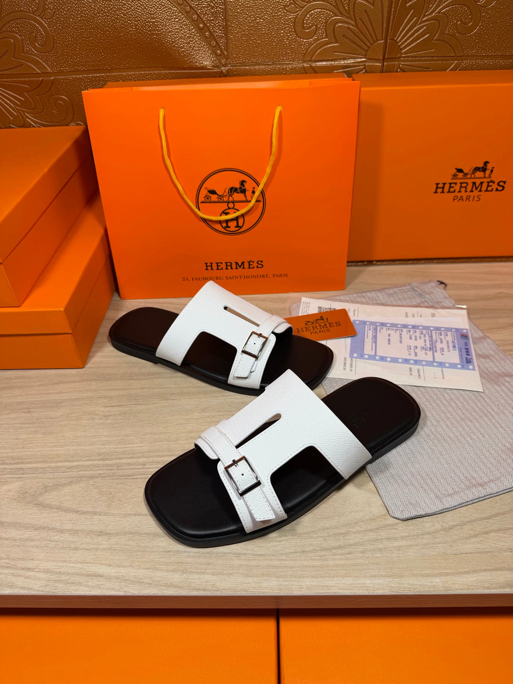 White slide sandals with two adjustable straps and silver buckles, black footbed