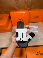 White slide sandal with metal buckle strap and black footbed