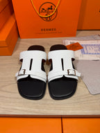 White slide sandals with two straps and metal buckle, black footbed