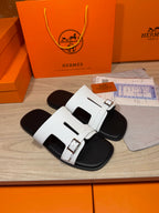 White slide sandals with double straps and metal buckles, black footbed