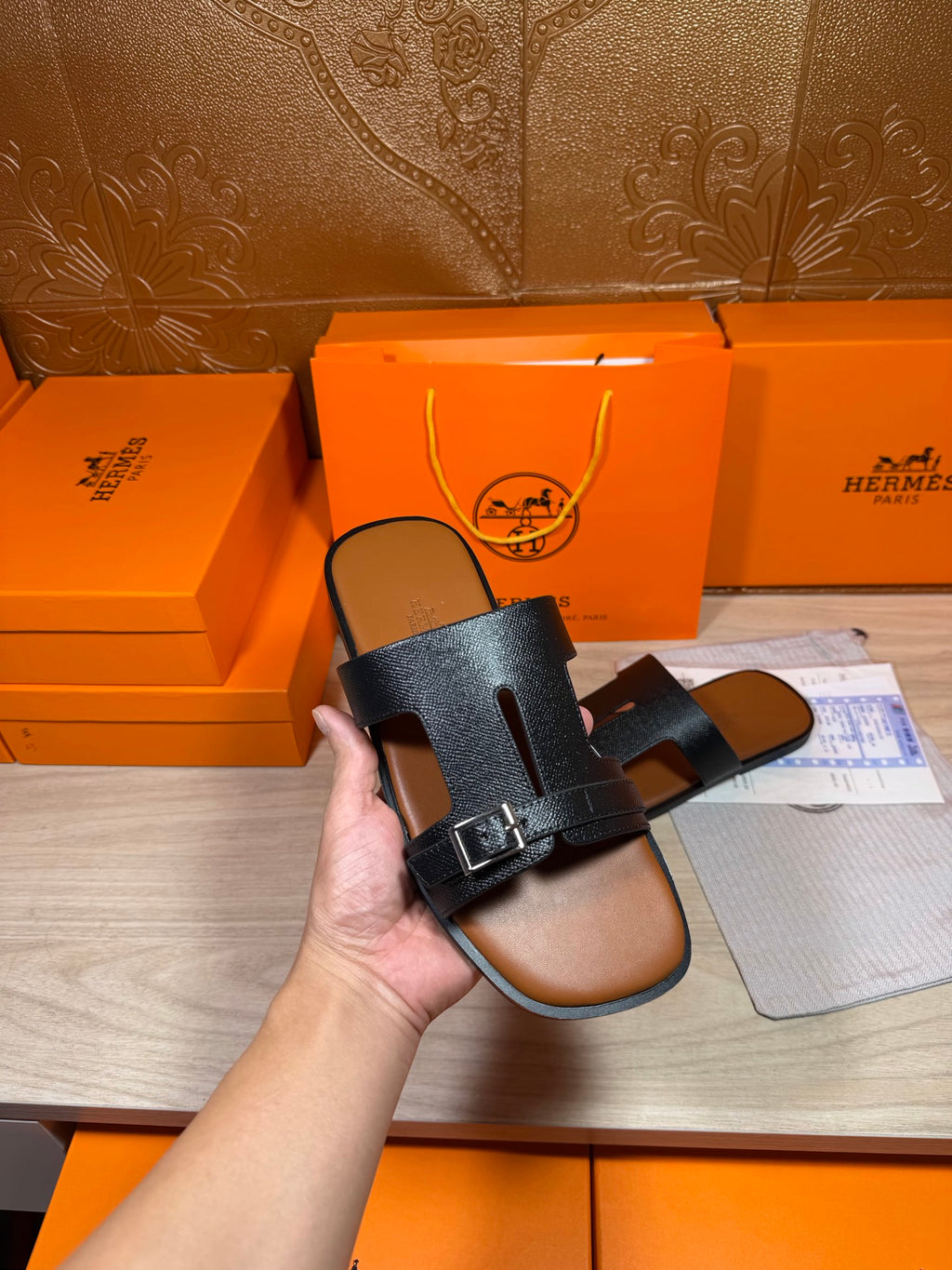 Hermes dark blue sandals held in hand, showing front cross straps and buckle detail