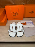 White slide sandals with two wide straps and silver-tone buckles