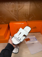 White slide sandals with two straps and buckle closure, held in hand