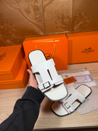 White slide sandals with adjustable buckle strap, held in hand