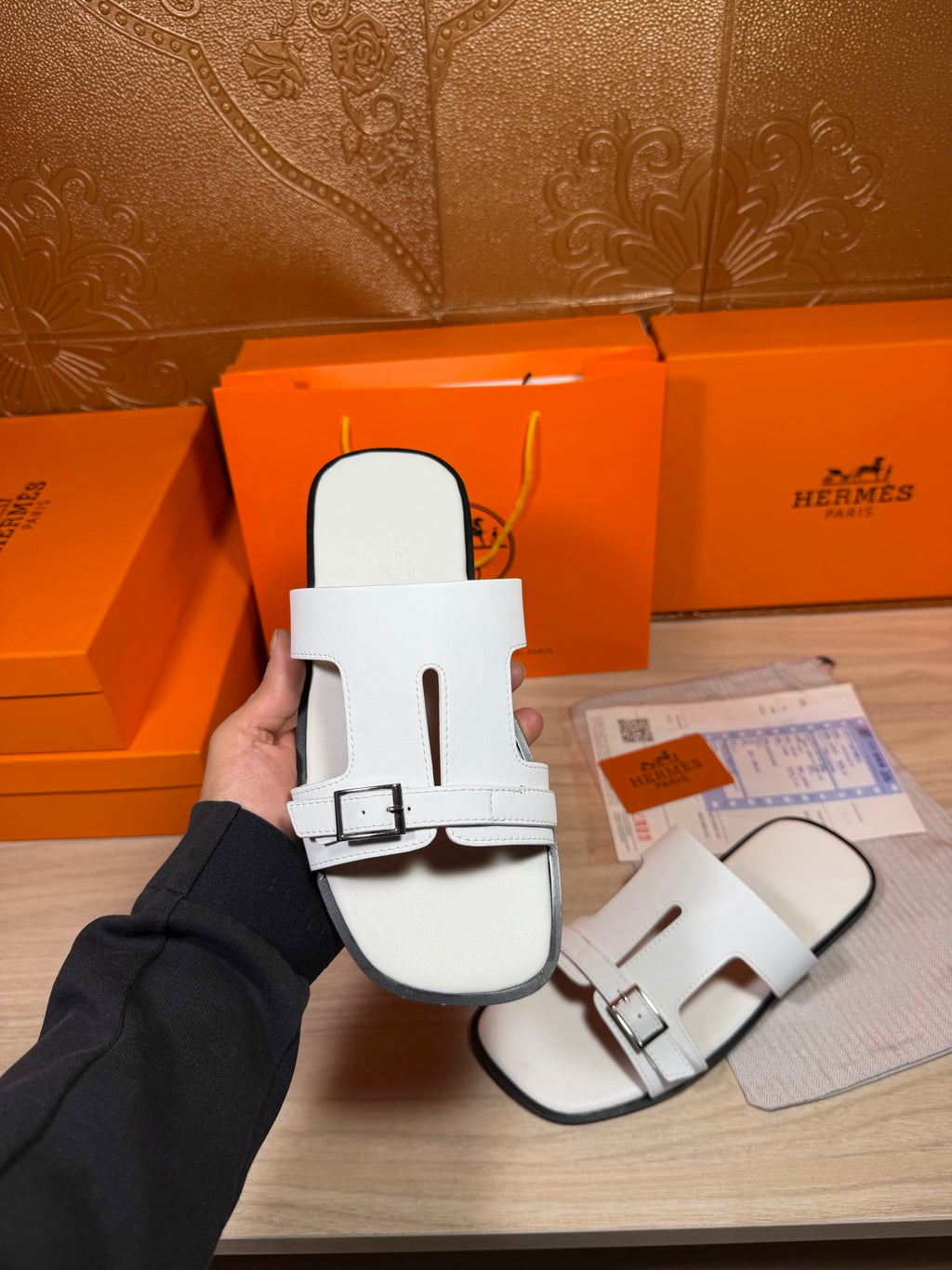 White slide sandals with wide top strap and buckle, held up for view