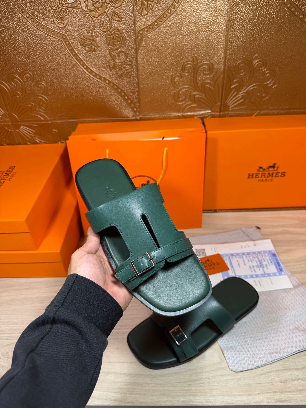Hermes teal-green leather slide sandals held up, featuring adjustable buckle straps