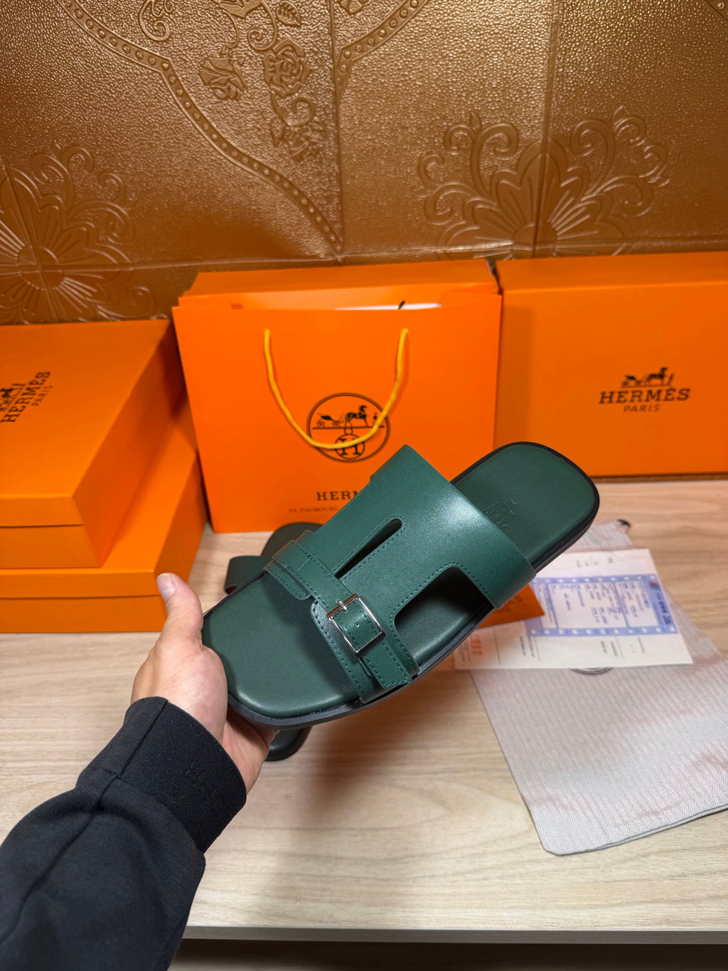 Hermes teal-green leather slide sandals held in hand, showing double buckle straps