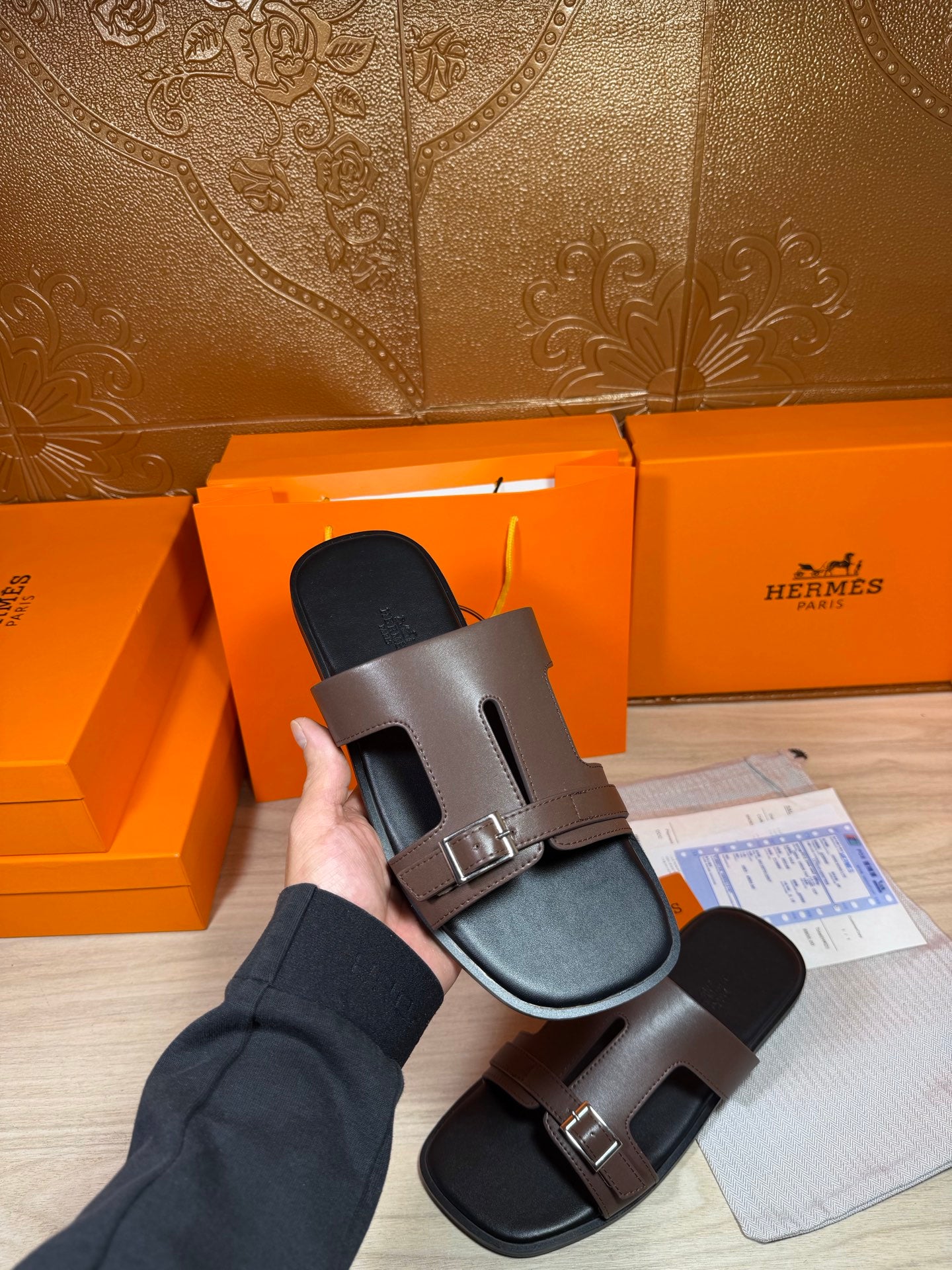 Brown leather slide sandals held in hand, open toe with double strap buckles