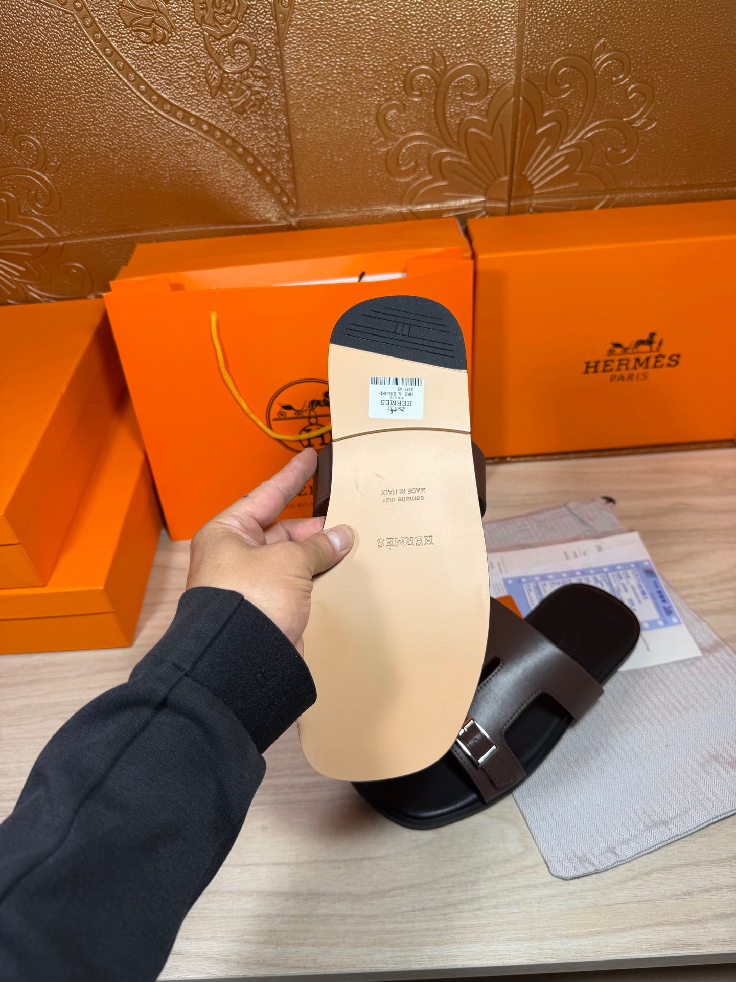 Brown leather slide sandal with strap buckle detail; tag and packaging visible