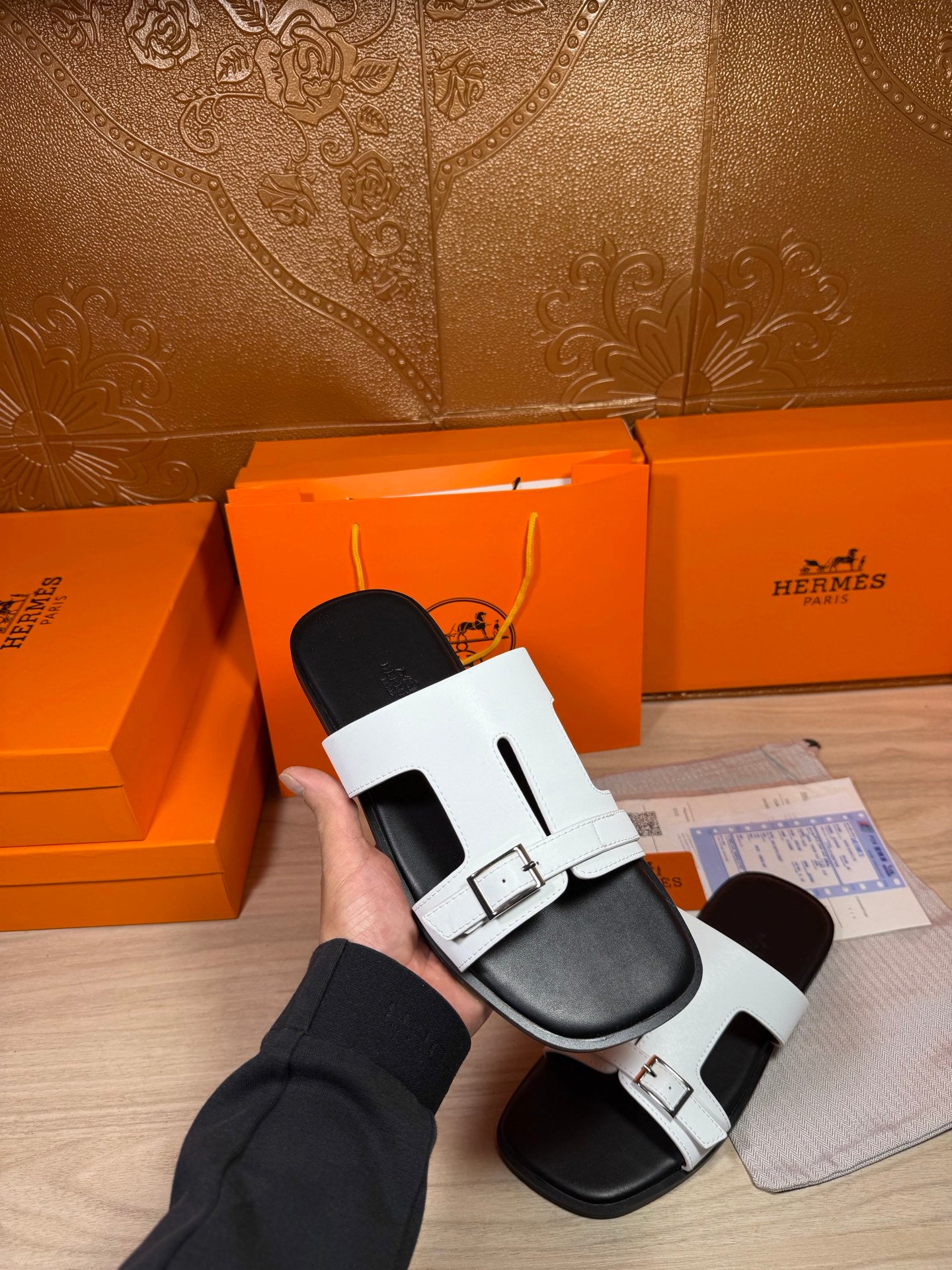 White Hermes slide sandals held in hand, with black footbeds and buckles