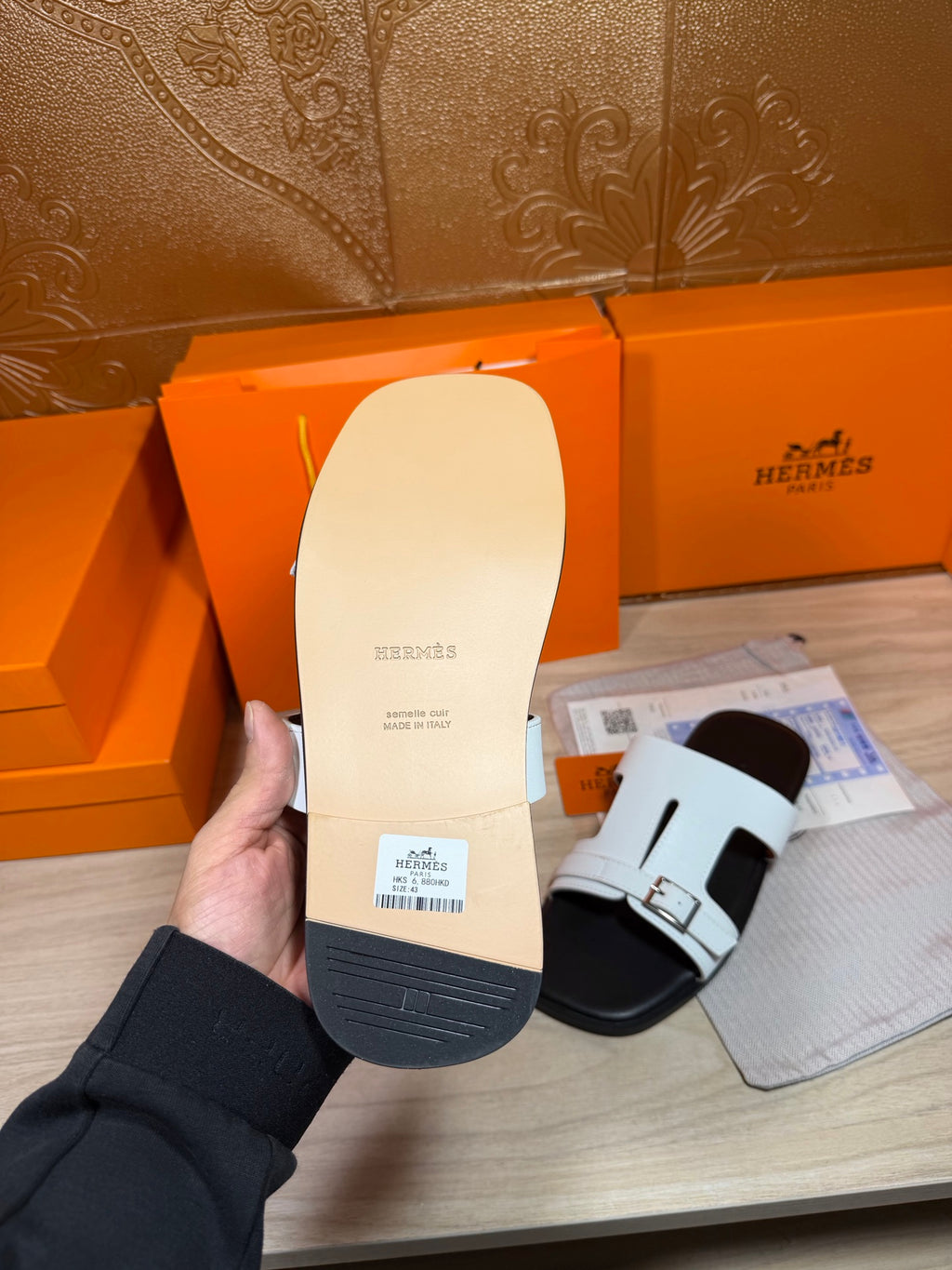 Sandal sole underside held by hand, white leather upper and dark rubber tread
