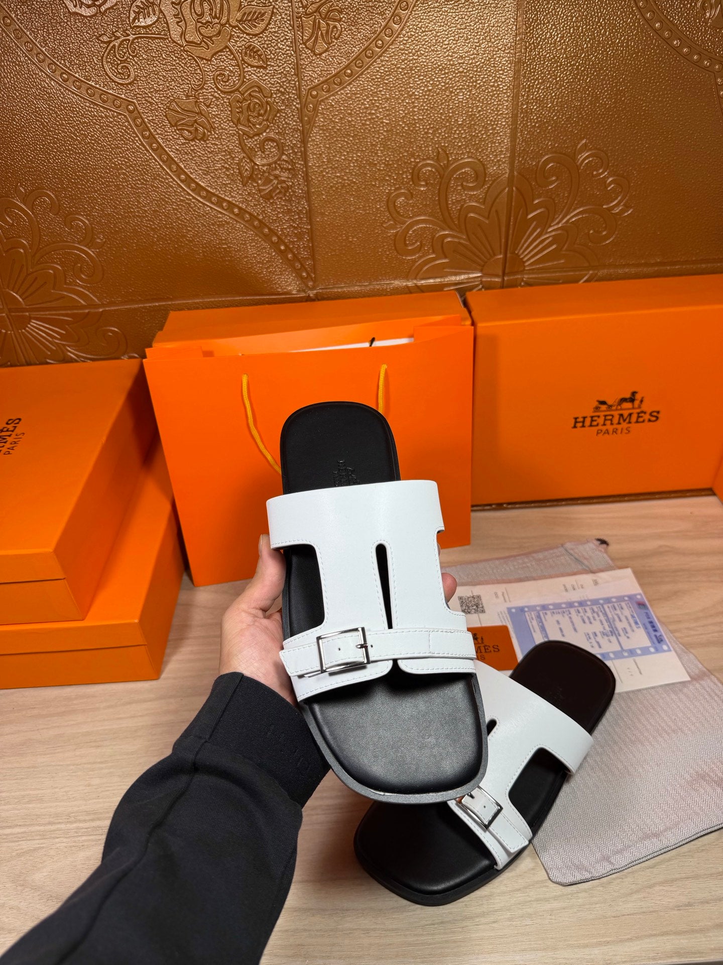 White Hermes slide sandals in hand, featuring metal buckle and black sole
