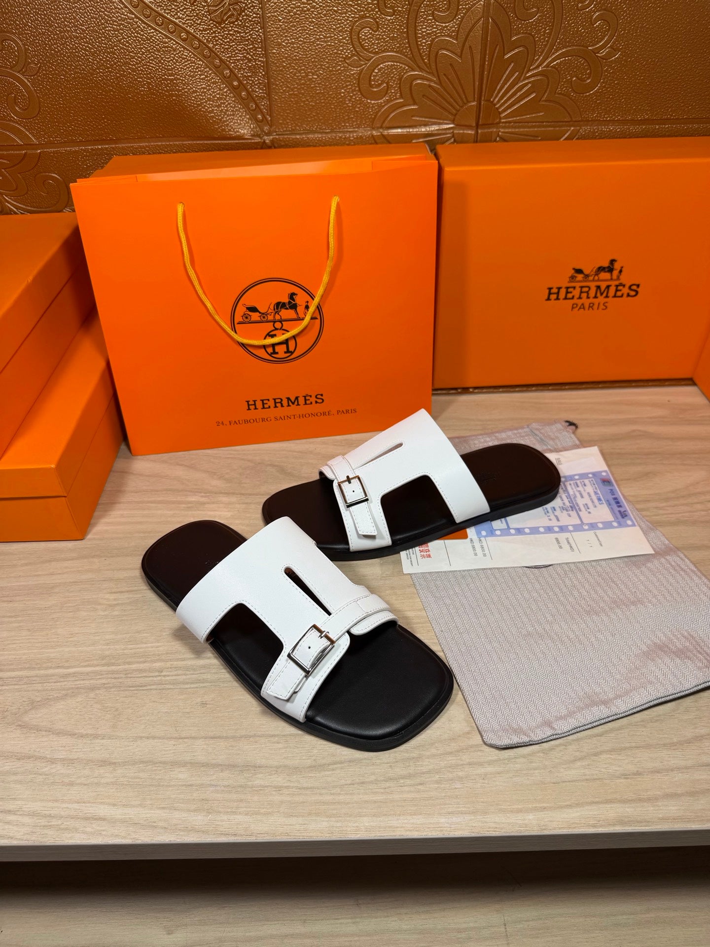 White Hermes buckle slide sandals with black footbed, showing strap details