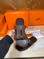 Brown leather slide sandal with single front buckle strap, held up