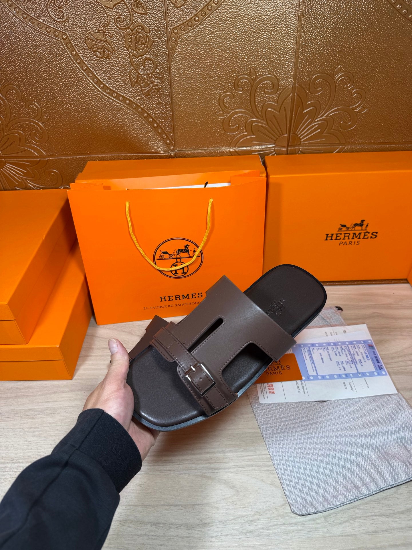 Brown leather slide sandal with front buckle strap, held at an angle