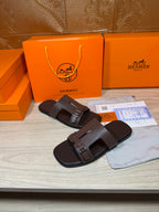 Brown leather slide sandals with two buckled straps, angled view