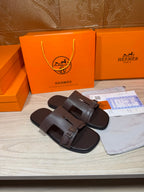 Brown leather slide sandals with two buckled straps on a flat surface