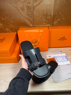 Black slide sandal held in hand, showing one strap and metal buckle