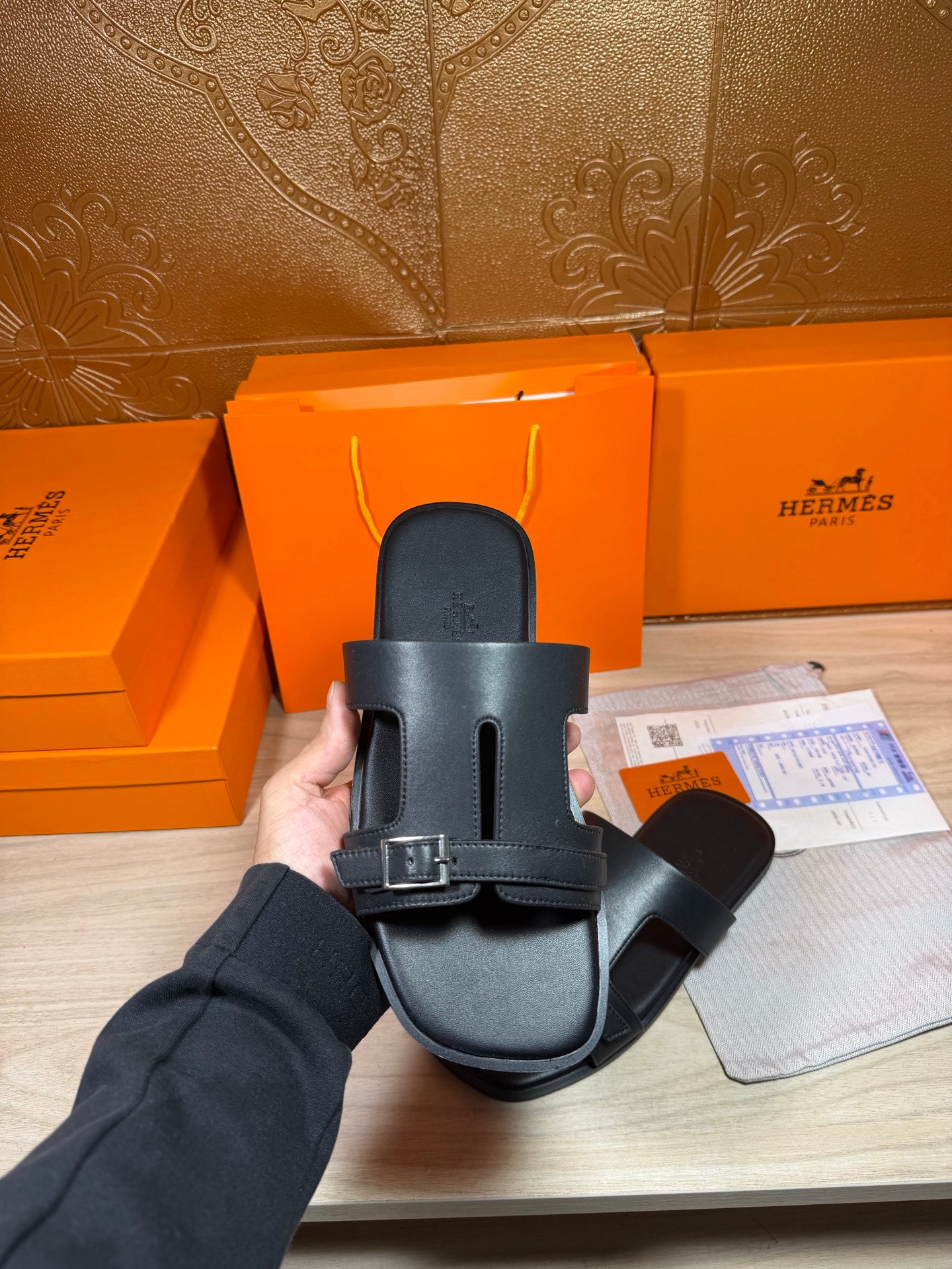 Black slide sandal held in hand, showing heel strap and metal buckle
