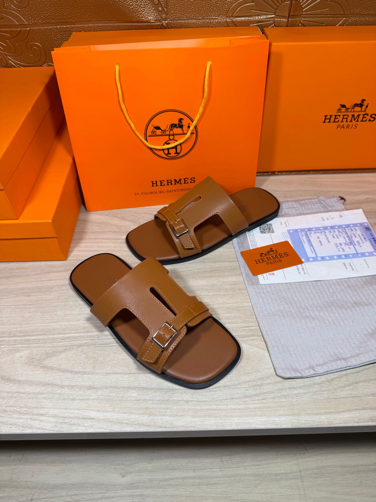Hermes tan leather sandals with metal buckle on front strap and open heel, angled view.