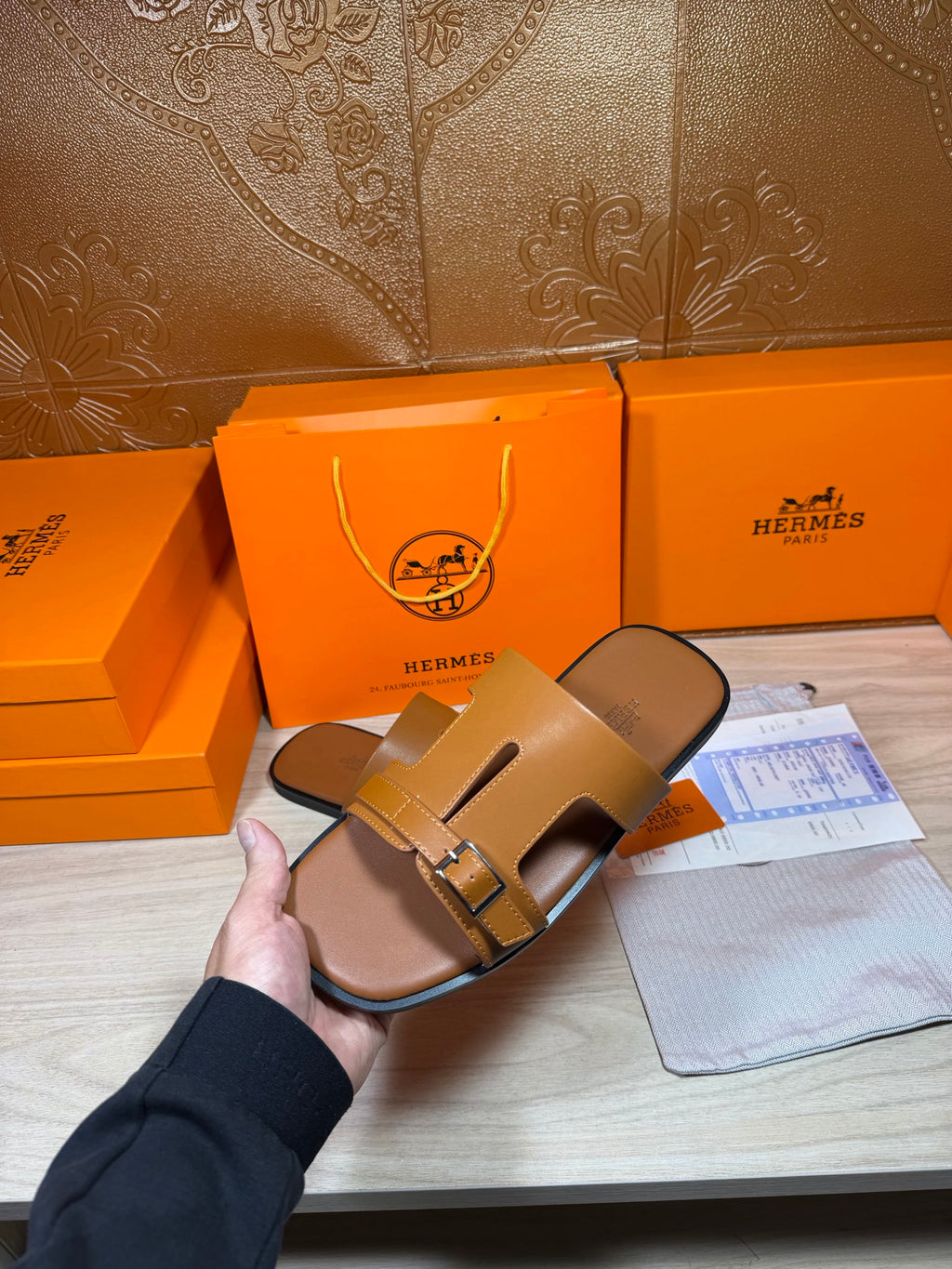 Hermes tan leather sandals held in hand, two straps with square metal buckle.